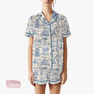 K&ouml;nnte beinhalten: Cremefarbenes Pyjama-Set mit blauem Pariser-Themen-Druck. Das kurz&auml;rmelige Oberteil und die Shorts zeigen Illustrationen des Eiffelturms, des Arc de Triomphe und Fahrr&auml;dern. Das Set ist mit blauen Paspeln versehen und hat eine Knopfleiste.