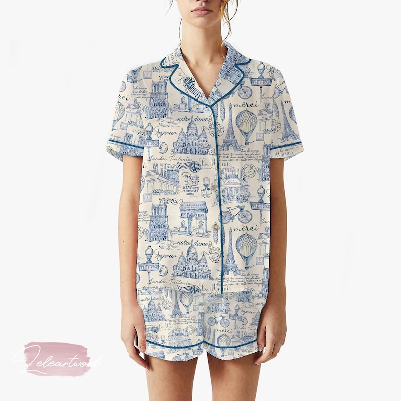 K&ouml;nnte beinhalten: Cremefarbenes Pyjama-Set mit blauem Pariser-Themen-Druck. Das kurz&auml;rmelige Oberteil und die Shorts zeigen Illustrationen des Eiffelturms, des Arc de Triomphe und Fahrr&auml;dern. Das Set ist mit blauen Paspeln versehen und hat eine Knopfleiste.