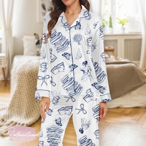 May include: White pajama set with a blue book, butterfly, and teacup pattern. The long-sleeved top and pants have blue trim. The pajama set is made of a soft, silky material.