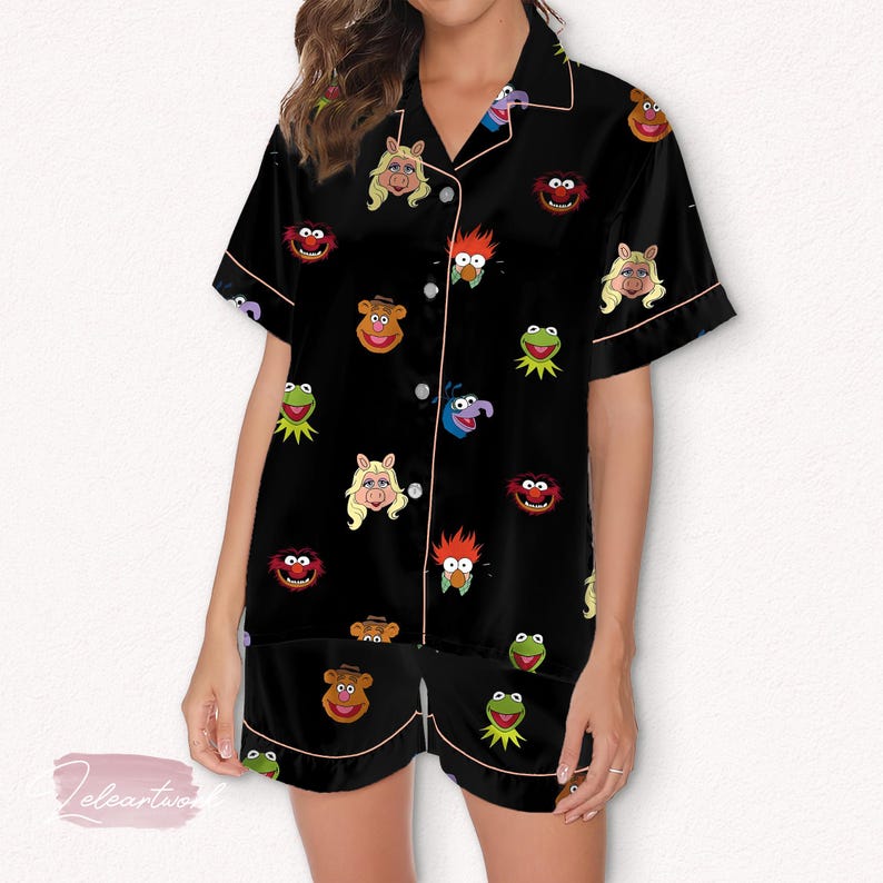 May include: Black pajama set featuring various Muppet characters. The short-sleeved top and shorts have a pink trim and button-up front. The Muppet characters include Kermit the Frog, Miss Piggy, Fozzie Bear, and others.