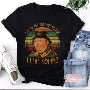 May include: Black t-shirt with a vintage-style graphic of a man in a military uniform. The graphic features a sunset background and the text "I know nothing I see nothing I hear nothing".