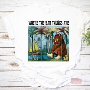 Könnte beinhalten: Weißes T-Shirt mit einer farbenfrohen Illustration aus "Wo die wilden Kerle wohnen". Das Design zeigt ein Monster, ein Segelboot und den Text "WHERE THE BAD THINGS ARE" in schwarzen Buchstaben. Das Shirt besteht aus einem weichen Material.