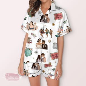 Puede incluir: Conjunto de pijama blanco con camisa abotonada y pantalones cortos. El conjunto presenta un patrón repetido de ilustraciones, incluyendo parejas, escenas de playa y elementos florales. El conjunto tiene ribete negro.