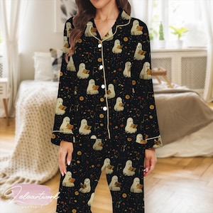 May include: Black pajama set featuring a repeating pattern of reading ghosts, orange dots, and small yellow circles. The long-sleeved top and pants have white trim and buttons. The pajamas are made of a soft, comfortable material.