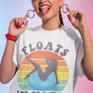 May include: White t-shirt with a vintage-style graphic of a woman sitting on a blue float with the text "FLOATS 'N HOES" in black.