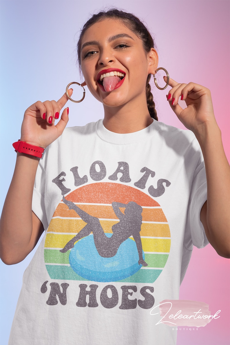May include: White t-shirt with a vintage-style graphic of a woman sitting on a blue float with the text "FLOATS 'N HOES" in black.