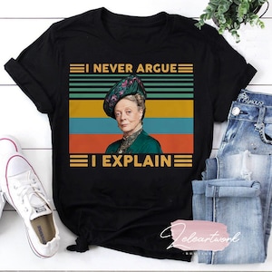 Könnte beinhalten: Schwarzes T-Shirt mit dem goldenen Text "I NEVER ARGUE I EXPLAIN". Das Shirt zeigt ein Bild einer Frau in grünem Kleid und Hut im Vintage-Stil, vor einem Hintergrund aus horizontalen Streifen in Türkis, Gold und Orange.
