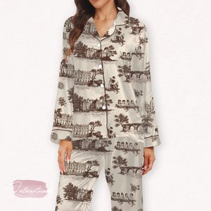 Peut inclure: Ensemble de pyjama crème avec un motif de toile de Jouy marron représentant des bâtiments, des arbres et des personnages. L'ensemble comprend un haut boutonné avec un col cranté et des manches longues, et un pantalon assorti.