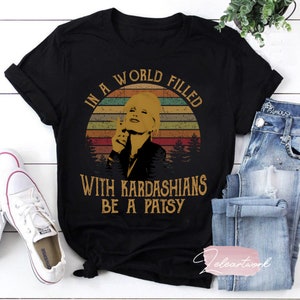 May include: Black t-shirt with a vintage-style graphic featuring a woman with blonde hair and the text "In a world filled with Kardashians be a Patsy".