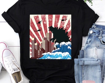 May include: Black t-shirt with a graphic of Godzilla standing in a city with a red, white, and blue sunburst background.