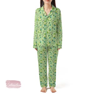 Può includere: Set pigiama verde con un motivo ripetuto di foglie e altre forme. La parte superiore a maniche lunghe ha un colletto e una chiusura con bottoni. I pantaloni sono lunghi e hanno un motivo abbinato. Il bordo è verde scuro.