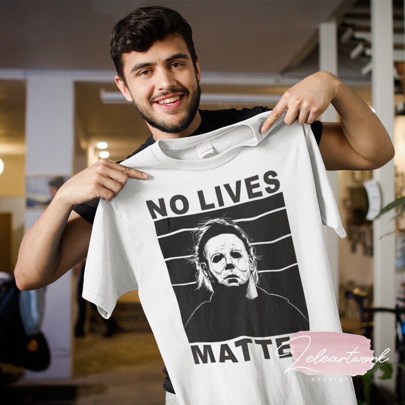 Puede incluir: Camiseta blanca con un gr&aacute;fico en blanco y negro de una figura enmascarada. El texto "NO LIVES MATTER" est&aacute; impreso en la camiseta.