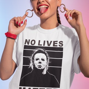 Puede incluir: Camiseta blanca con un gr&aacute;fico en blanco y negro de Michael Myers de la pel&iacute;cula Halloween. El texto "NO LIVES MATTER" est&aacute; impreso sobre el gr&aacute;fico.