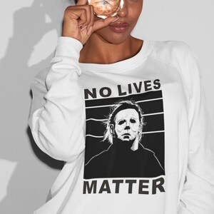Puede incluir: Sudadera blanca con un estampado gr&aacute;fico en blanco y negro de un personaje de pel&iacute;cula de terror con el texto "NO LIVES MATTER".