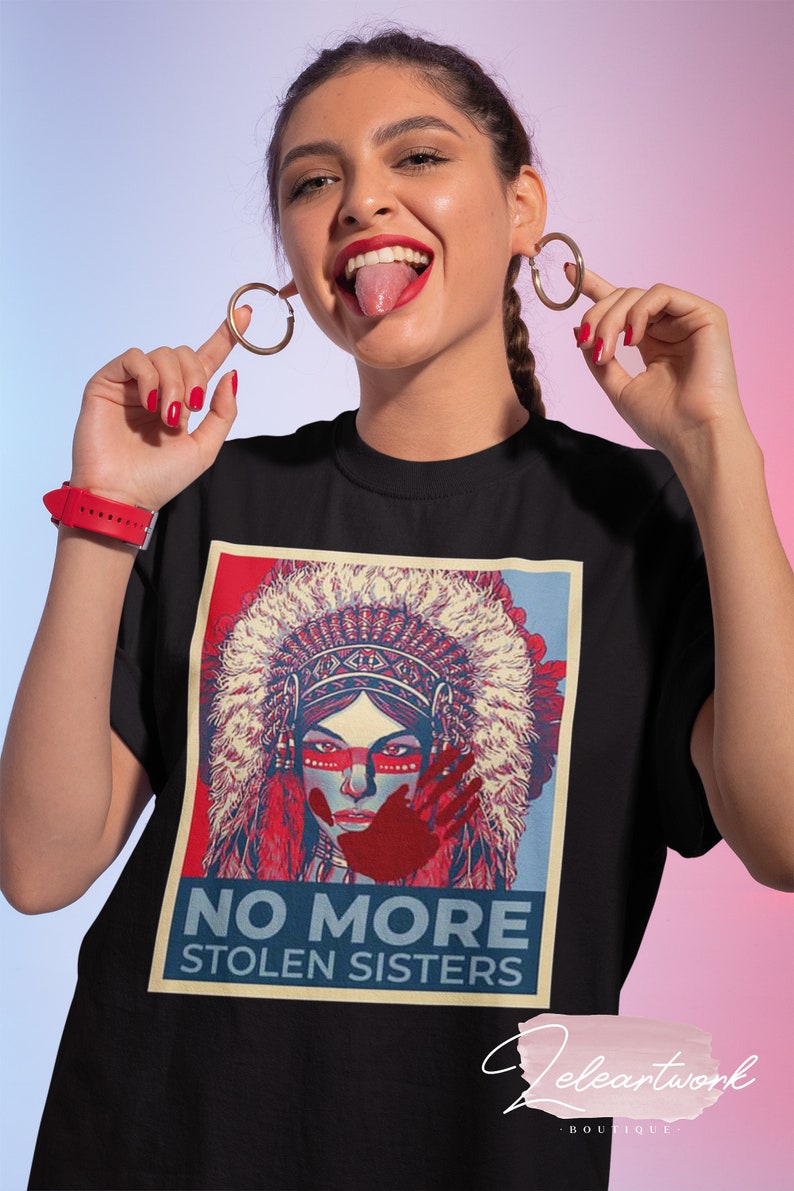 May include: Black t-shirt with a graphic of a Native American woman in a headdress, red face paint, and a red handprint. The text "NO MORE STOLEN SISTERS" is below the image. The woman in the image is wearing gold hoop earrings.