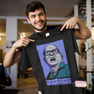 May include: Black t-shirt with a cartoon illustration of a man with glasses and a surprised expression. The text "Emotional Vampire" is printed below the image.