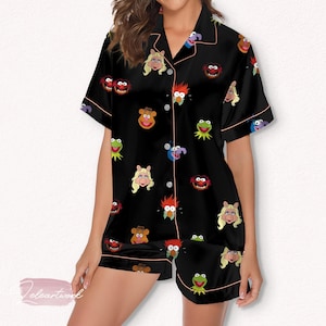 May include: Black pajama set featuring a pattern of Muppet characters. The short-sleeved top and shorts have pink trim. The Muppet faces are in various colors, including green, red, and pink.