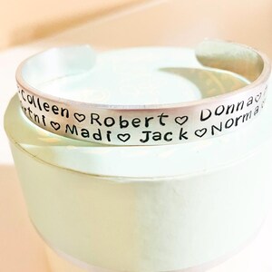 May include: Silver bracelet with the names Colleen, Robert, Madi, Jack, Donna, and Norma engraved on it, separated by heart symbols.