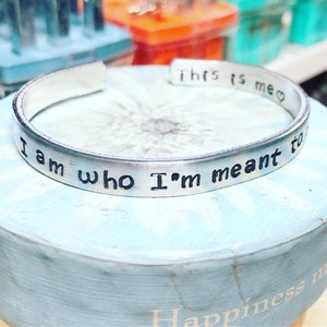 May include: A silver metal bracelet with the inscription "I am who I'm meant to be".