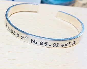 May include: Silver bangle bracelet with engraved coordinates: 43.03 82° N. 87. 92 98° W.