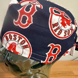 May include: A navy blue surgical scrub cap featuring the Boston Red Sox logo in red and white. The cap has a repeating pattern of the team's logo and lettering. The cap is made of a soft, likely cotton, fabric.