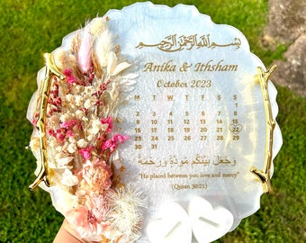 May include: A white circular resin tray with a gold-colored branch design and a calendar for October 2023. The tray features dried flowers and a quote in Arabic script with an English translation: "He placed between you love and mercy" (Quran 30:21).