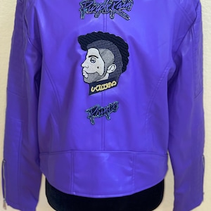 May include: Purple leather jacket with a Prince inspired design. The jacket features a purple rain patch, a Prince portrait patch, and a gold chain patch.