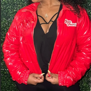 Può includere: Una giacca a vento rossa lucida con chiusura a zip e un logo "San Francisco" sul lato destro.