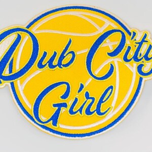 Könnte beinhalten: Ein gestickter Aufnäher in Gelb und Blau mit einem Basketball-Design und dem Text "Dub City Girl".