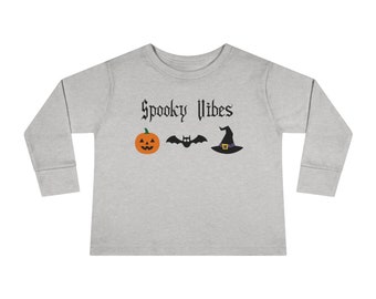 Könnte beinhalten: Ein graues Langarmshirt mit dem Text "Spooky Vibes" in Schwarz. Das Shirt zeigt eine Grafik mit einem Kürbis, einer Fledermaus und einem Hexenhut.