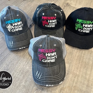 May include: Four distressed trucker hats with the text "MESSY HAIR DON'T CARE" embroidered on the front. The hats are in black, gray, and denim blue, with the text in various colors. The hats have a mesh back and a curved brim.