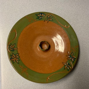 May include: A brown ceramic serving dish with a green rim and floral design. The dish has a raised center for serving dips or sauces.