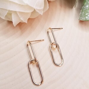 May include: A pair of gold-toned earrings with a double chain link design. Each earring features two oval-shaped links.