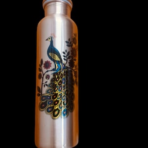 May include: A cylindrical copper water bottle featuring a metallic finish and a screw-top lid. The exterior is decorated with a colorful graphic print of a peacock perched on a branch, displaying its detailed plumage in shades of blue and gold.