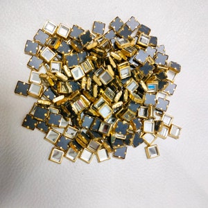 May include: A pile of small, square, mirrored tiles with gold trim and black backing. The tiles are scattered on a white surface.
