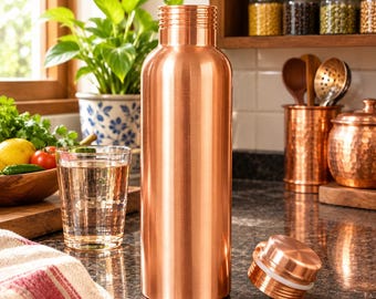 May include: A tall, cylindrical copper water bottle with a smooth, polished metallic finish and a matching screw-top lid resting beside it. The bottle features a narrow neck with horizontal ridges and a wide, flat base, reflecting light on its surface.
