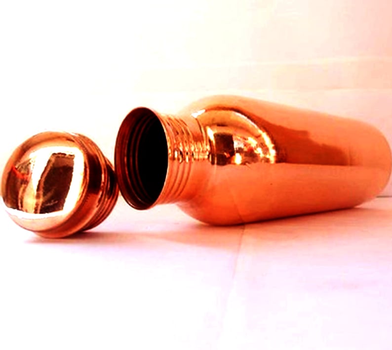 May include: A copper water bottle with a lid. The bottle is shiny and has a rounded shape.