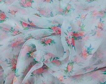 Puede incluir: Una tela transparente de color azul claro con estampado floral. Las flores son de color rosa, blanco y verde. La tela es translúcida y tiene una textura delicada.