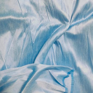 Puede incluir: Primer plano de una tela azul claro con un brillo sedoso. La tela está drapeada y doblada, creando sombras y reflejos que enfatizan su textura. El color es un azul pastel suave y la tela parece ligera.