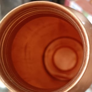 May include: A copper water bottle with a wide mouth opening. The inside of the bottle is shiny and smooth.