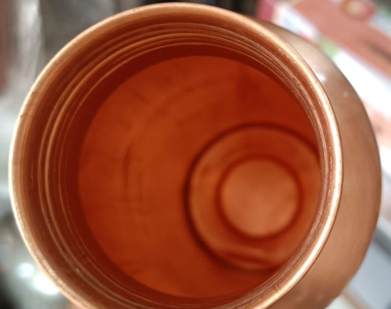 May include: A copper water bottle with a wide mouth opening. The inside of the bottle is shiny and smooth.