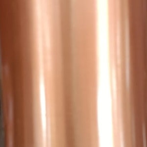 May include: A copper water bottle with a shiny, polished finish. The bottle is tall and cylindrical with a narrow neck.