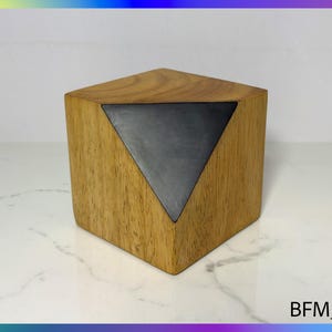 Op de afbeelding: Een houten kubus met een driehoekige inleg van donkergrijs materiaal. De kubus heeft een natuurlijke houten afwerking.