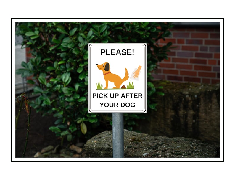 May include: A white sign with black text and a cartoon dog on it. The sign reads "PLEASE! PICK UP AFTER YOUR DOG". A cartoon hand is holding a plastic bag. The sign is mounted on a metal pole.