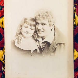 May include: Black and white vintage photograph of a man and a young girl. The man is wearing a dark suit and a white shirt with a tie. The girl is wearing a dark dress with a white collar. The photo is signed "Laumer W.J. Scanlan. New York."