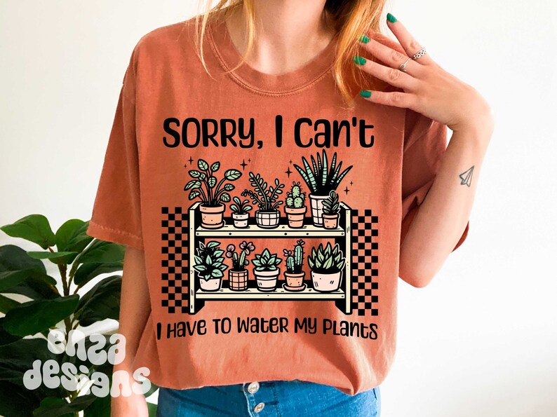 Puede incluir: Una camiseta de color &oacute;xido con el texto "Lo siento, no puedo, tengo que regar mis plantas". El texto est&aacute; en negro y est&aacute; sobre un dibujo de una estanter&iacute;a con plantas en macetas.