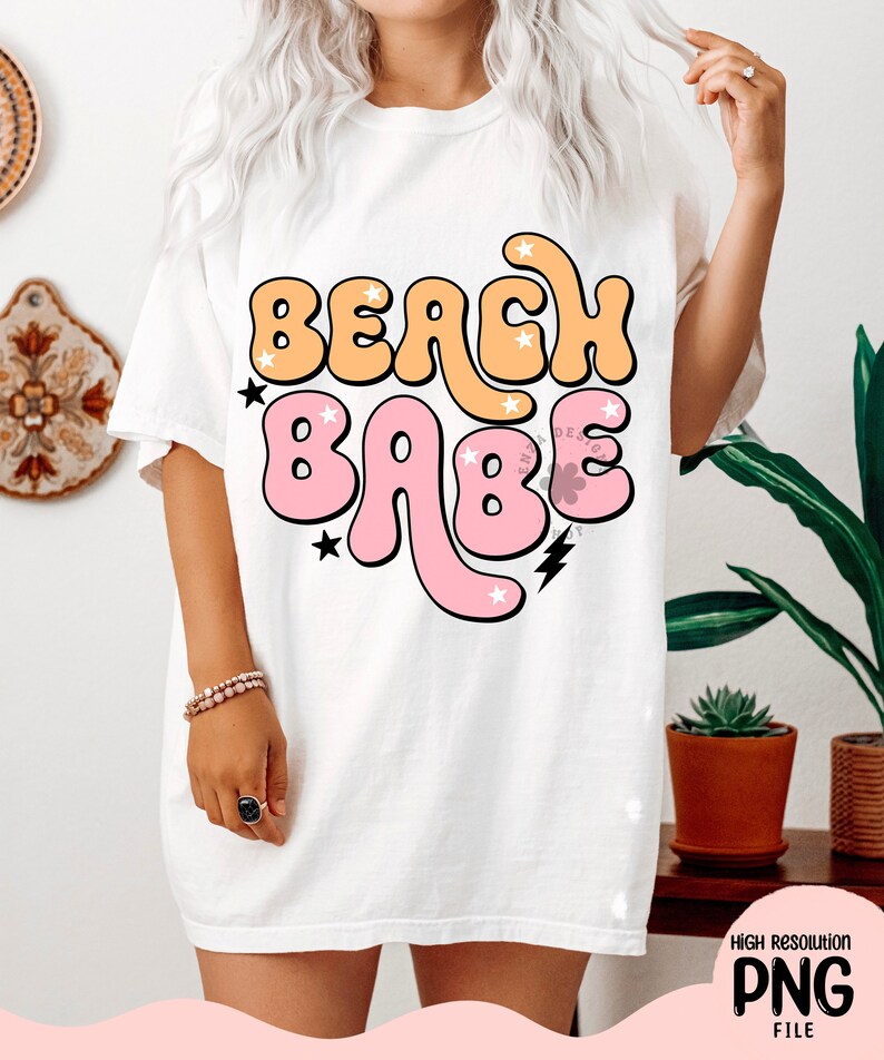 May include: White t-shirt with a graphic design that says "Beach Babe" in pink and orange bubble letters with stars and lightning bolts.