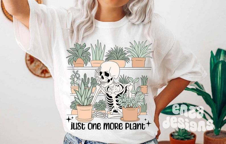 May include: White t-shirt with a graphic of a skeleton sitting among potted plants on a shelf. The text "just one more plant" is printed below the graphic.