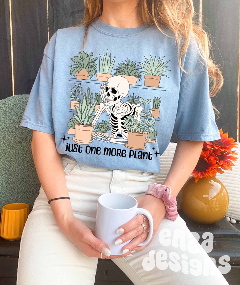 May include: A light blue t-shirt with a graphic of a skeleton surrounded by potted plants. The text "just one more plant" is printed below the graphic.
