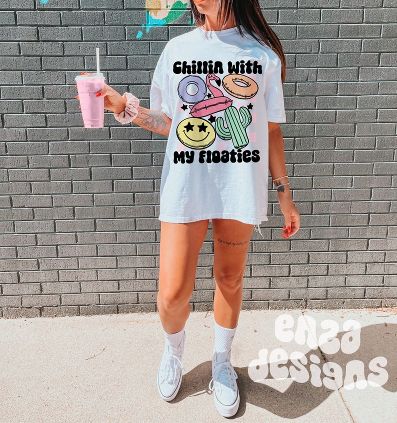 May include: White oversized t-shirt with the text "Chillin with my floaties" and a graphic of a flamingo, donut, cactus, and smiley face float.